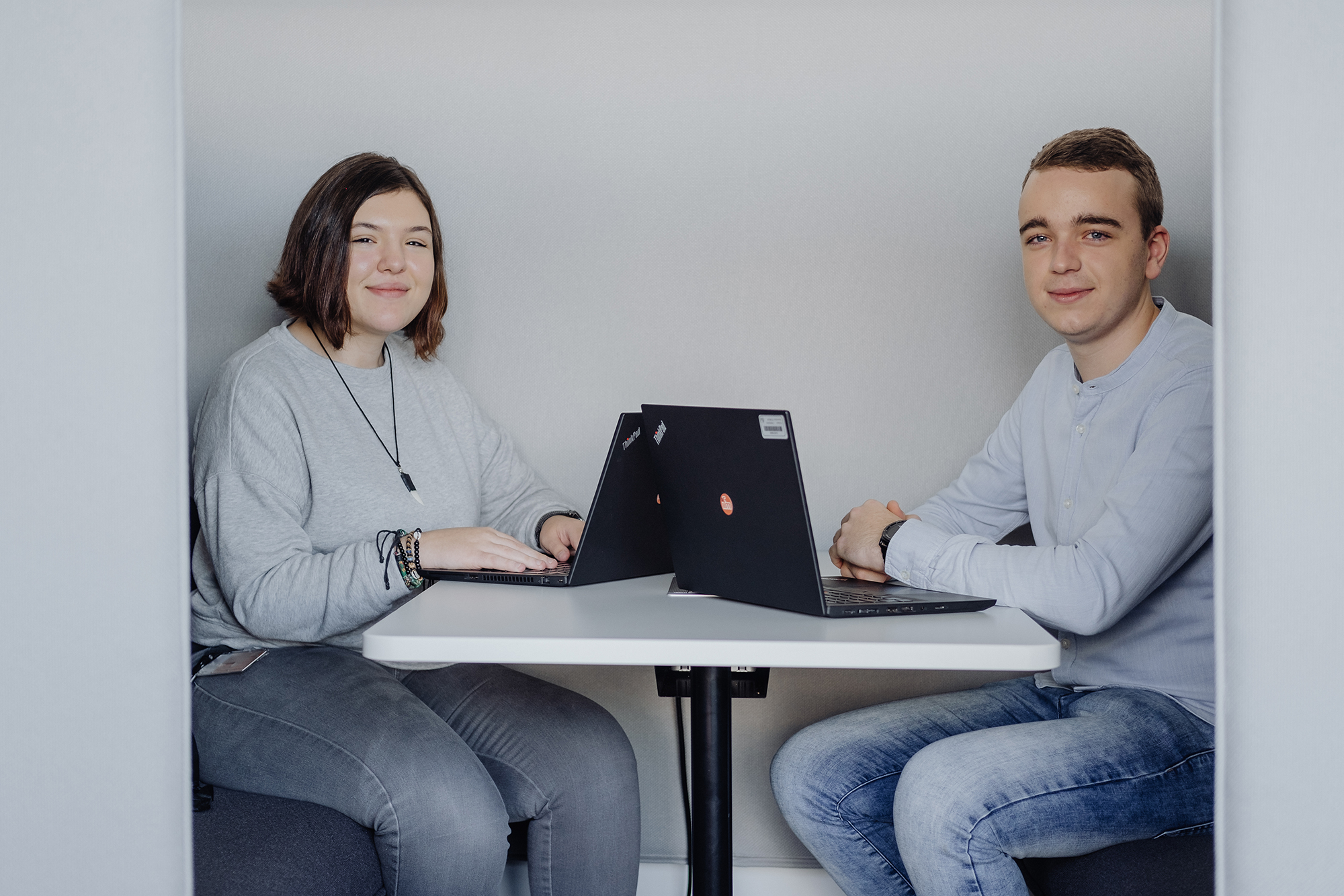 Zwei Mitarbeiter:innen sitzen zusammen an einem Tisch und arbeiten an ihren Laptops.